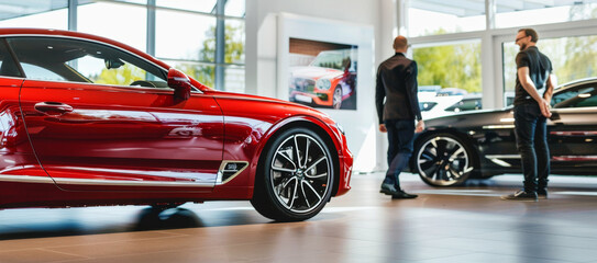 Stylish red car on exhibit with shoppers in dealership setting