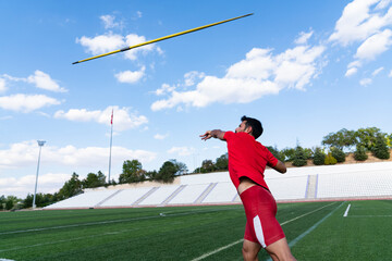 An athletic man throws the javelin in the stadium.