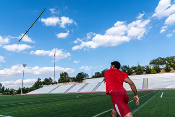 An athletic man throws the javelin in the stadium.