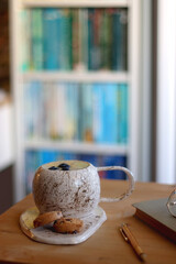 Cup of blueberry and banana smoothie, chocolate chip cookies, book, pen and reading glasses on the table. Colorful bookshelf in the background. Selective focus.