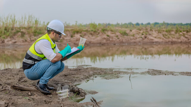 Environmental engineer Sit down next to a well while holding the plastic glass in his left hand and take a note the result of analysing check the quality and contaminants in the water source.