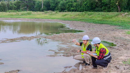 Two of environmental engineer Sit down next to a well while holding the plastic glass that fill with the water sample and check water quality and contaminants in the water source.