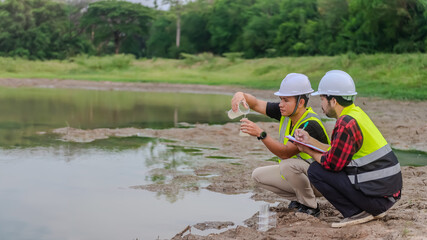 Two of environmental engineer Sit down next to a well and try to pouring the water from the plastic glass to the experiment tube to analysing check the quality and contaminants in the water source.