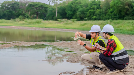 Two of environmental engineer Sit down next to a well and try to pouring the water from the plastic glass to the experiment tube to analysing check the quality and contaminants in the water source.