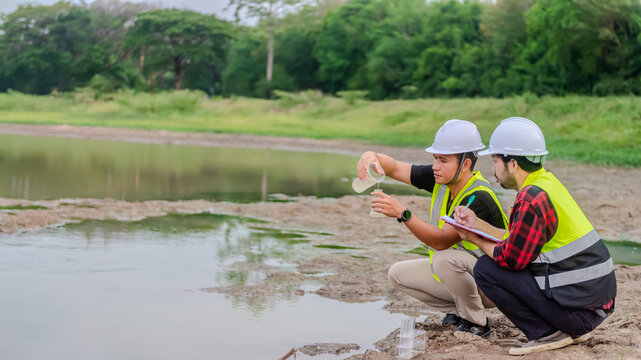 Two of environmental engineer Sit down next to a well and try to pouring the water from the plastic glass to the experiment tube to analysing check the quality and contaminants in the water source.