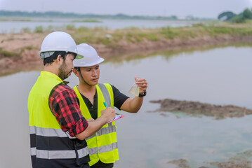 Two of environmental engineer stand next to a well while holding an experiment tube that fill with...