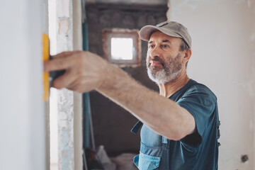 Man plastering the walls with finishing putty in the room with putty knife or spatula. Repair work,...