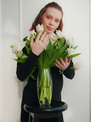 Pregnant woman with a hairstyle and makeup on her face in a black tight dress with white tulips