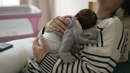 Mother holding newborn baby on chest while taking a nap, woman laid in bed holding infant tight on...