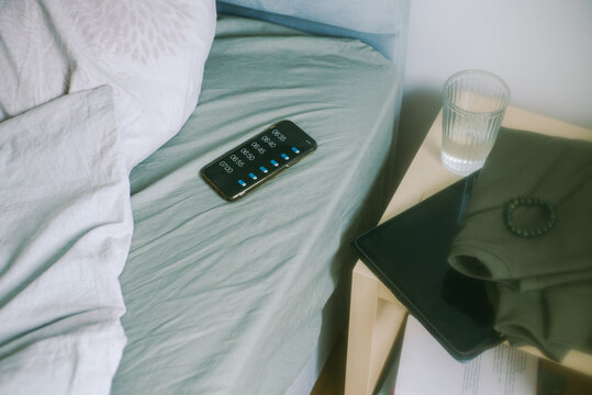A smartphone with active alarms lies on the bed  next to the pillow. 