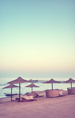 A tranquil beach with sun loungers and umbrellas at sunset, color toning applied, Egypt.