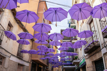 Multitude of purple umbrellas hanging in the middle of the street decorating.