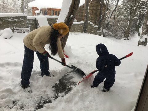 Mother and son clean sidewalks with snow