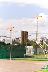 Tablica kosza do koszykówki wiszącego nad boiskiem, w tle wysokie budynki oraz dwa dźwigi  © Piotr