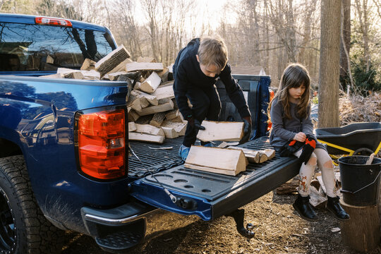 children helping with to stack firewood in backyard
