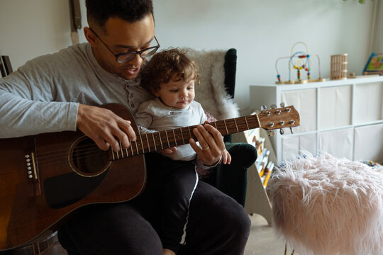 Toddler learning guitar with an adult indoors