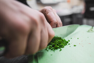 Close-up of hands finely chopping fresh herbs on a green cutting board, highlighting culinary skills and fresh ingredients