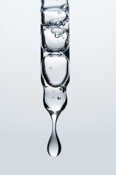 Clear glass pipette with a drop of cosmetic product falling down. 