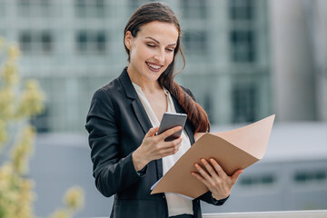 business woman with document folder on the street looking at mobile phone