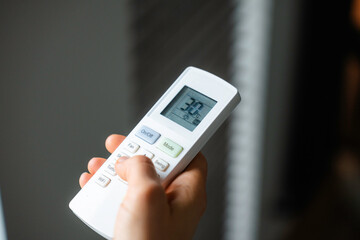 The woman controls the air conditioner using the remote control
