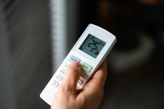 The woman controls the air conditioner using the remote control