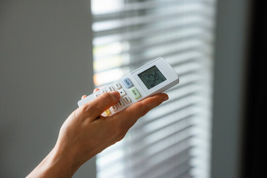 The woman controls the air conditioner using the remote control