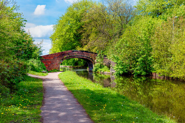 Historic brick bridge over serene canal with lush trees on a bright spring day