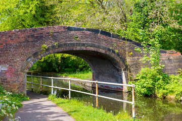 Historic arched brick bridge over tranquil canal with lush greenery on a bright summer day