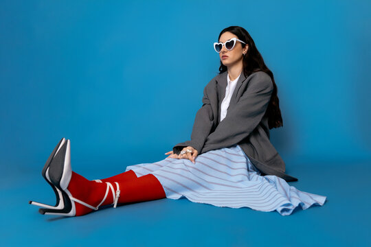 Female model with sunglasses and strap sandals sitting on blue surface