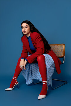 Stylish female mode sitting on chair in studio and looking at camera