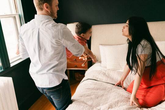 father holding toddler son and playing on the bed in bedroom