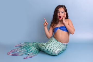 A surprised girl in a mermaid costume sits on a blue background