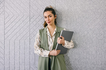 Confident businesswoman holding laptop against patterned wall