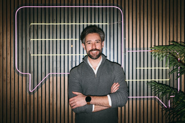 Smiling man with neon chat bubble on wooden background