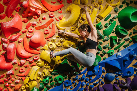 Skilled climber bouldering on a rainbow colored  indoor climbing wall