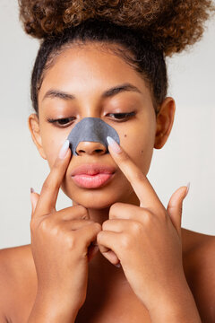 A woman is applying a black patch to her nose