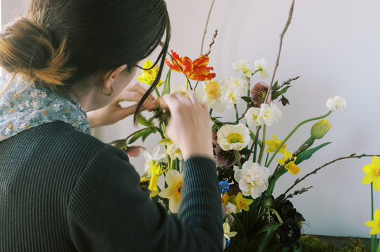 florist making an arrangement of spring florals indoors on dresser