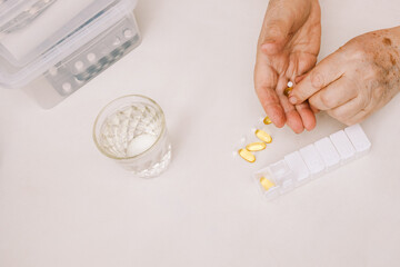 The hands of a man putting vitamins and supplements in a pillbox.