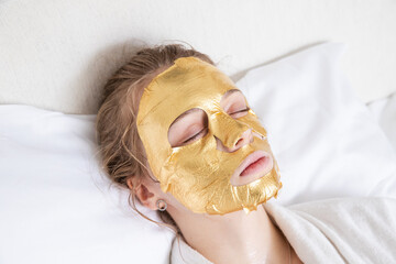 Girl lying in spa salon with golden cosmetic facial mask