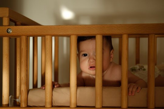 Little baby in a wooden cot in dark room