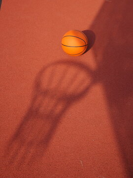 A basketball is sitting on a court with a shadow of a basketball hoop
