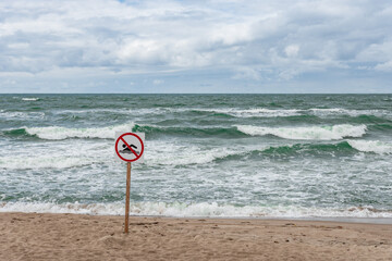 no swimming sign at an empty beach with rough wavy sea in a background