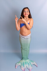 A beautiful child girl in a mermaid costume stand on a blue background