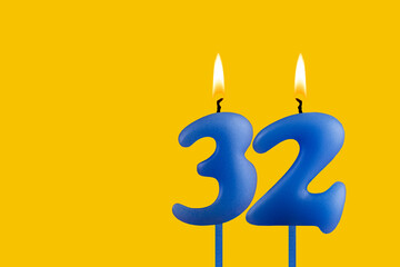 Blue birthday candle on yellow background - Number 32