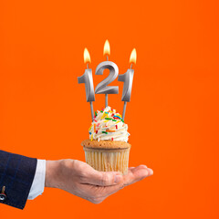 The hand that delivers cupcake with the number 121 candle - Birthday on orange background