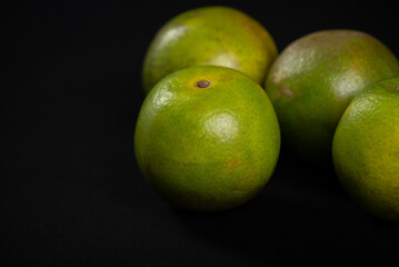 Close-up of four green oranges on a black background.