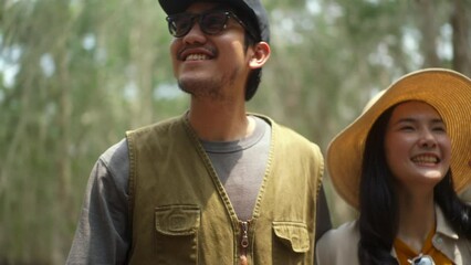 Happy asian couple traveling and looking around botanic natural forest during walking together in summer, young joyful male and female relaxing on vacation, concept of people enjoy outdoor lifestyle
