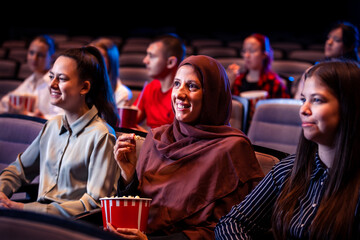 Hijab muslim woman watching a movie in cinema with her friends. Eating popcorn and enjoying
