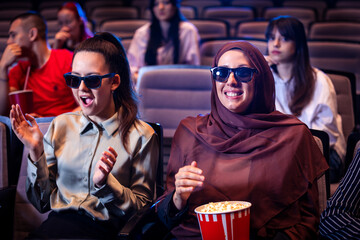 Hijab muslim woman watching a 3d movie in cinema with her friends. Eating popcorn and enjoying.