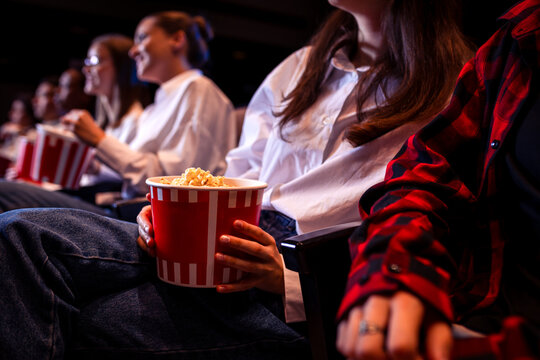 People are watching a movie in cinema. They are eating popcorn and drinking juices
